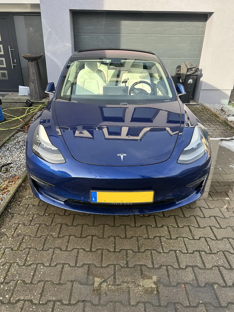 Front view of a blue Tesla parked on a driveway in front of a closed garage door.