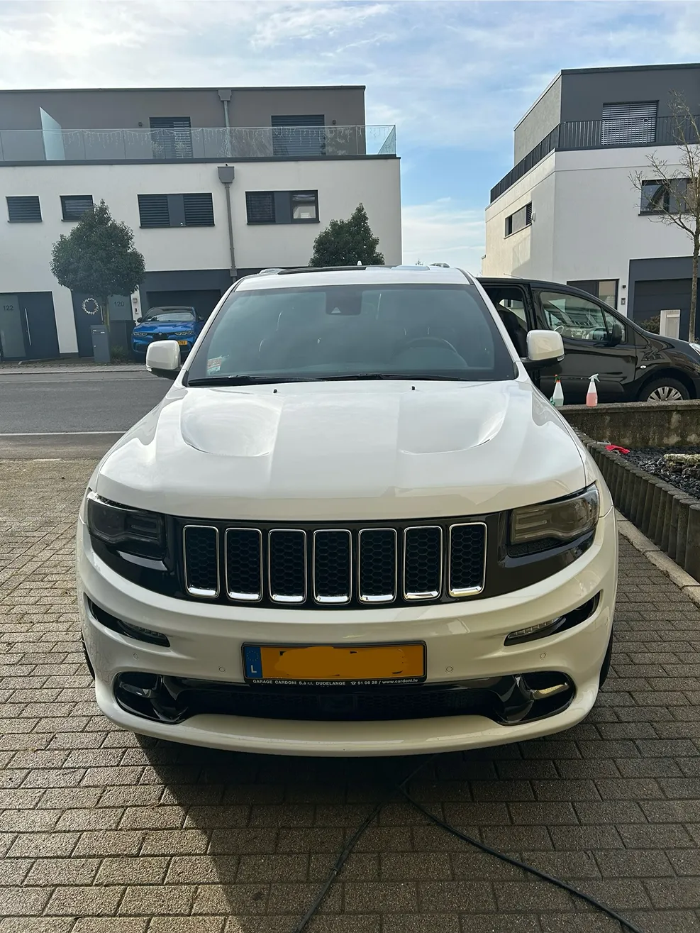 Front view of a white Jeep SUV parked on a driveway in a residential area with modern houses in the background.