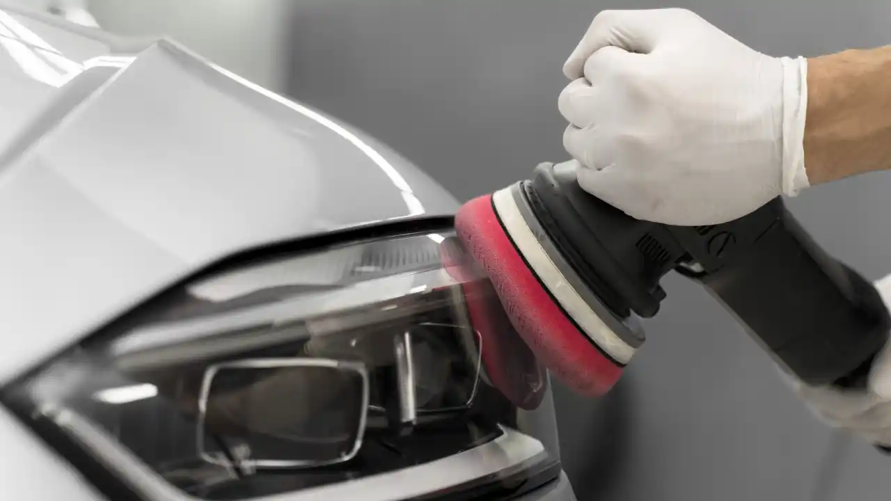 Gloved hand using a polishing machine to restore the surface of a car's headlamp.